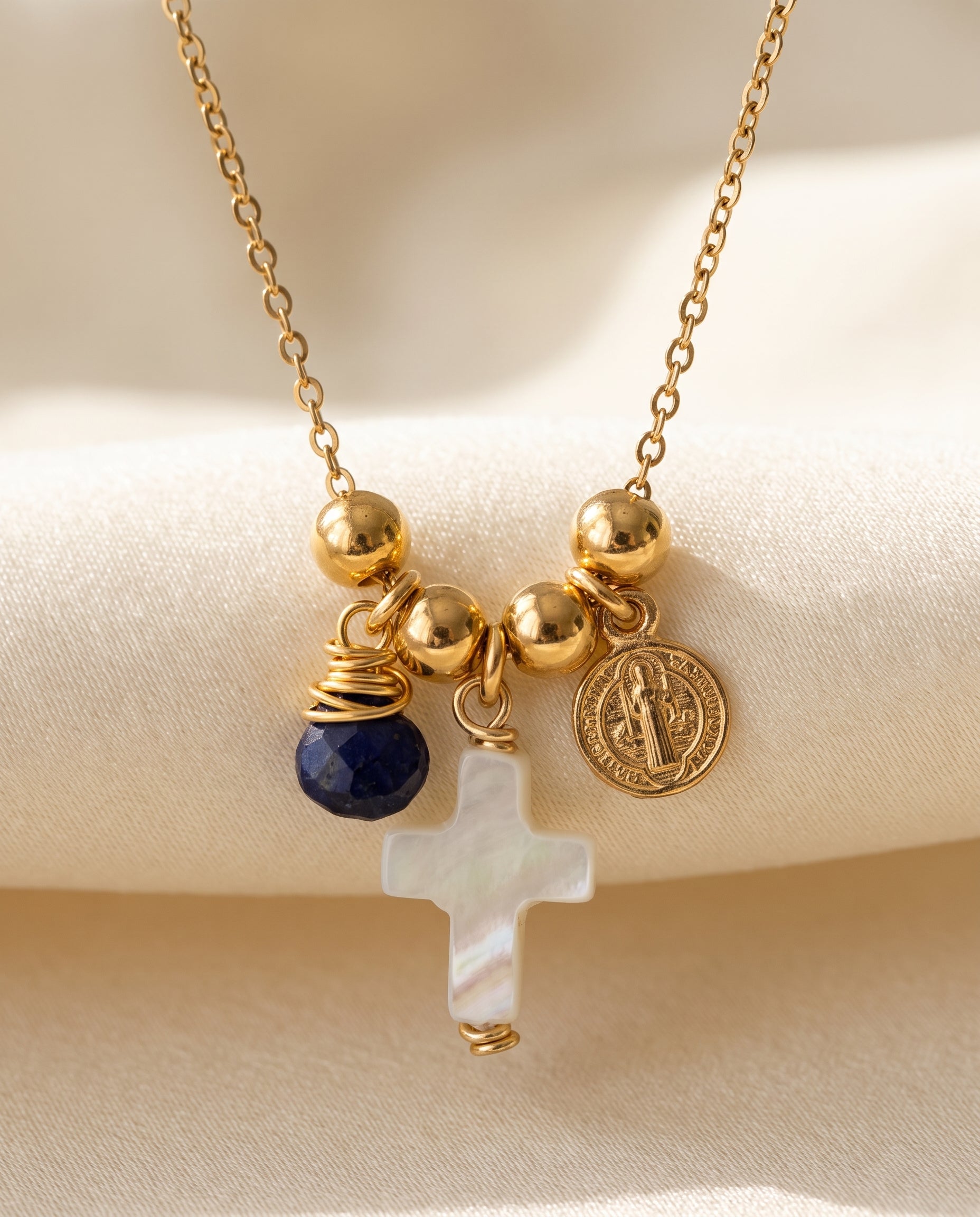 Detalle de la cruz de concha nácar, la medalla de San Benito chapada en oro y la piedra azul del collar Perla Santa