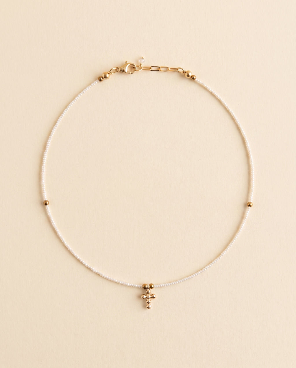 Collar de perla natural blanca con cruz de chapa de oro sobre fondo crema, Perla Santa