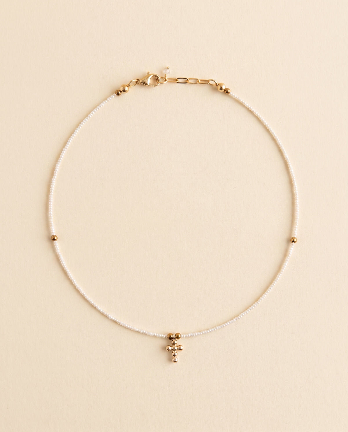 Collar de perla natural blanca con cruz de chapa de oro sobre fondo crema, Perla Santa