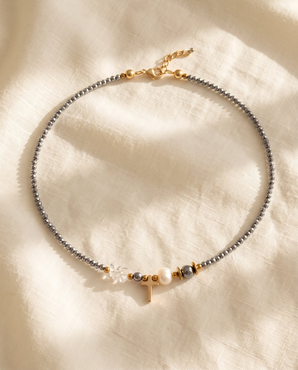 Collar de cristal facetado con cruz dorada y perla de Perla Santa sobre lino natural color crema