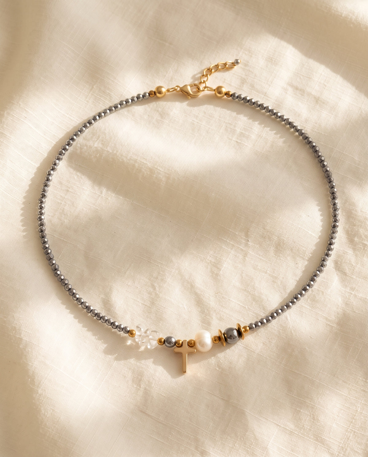 Collar de cristal facetado con cruz dorada y perla de Perla Santa sobre lino natural color crema