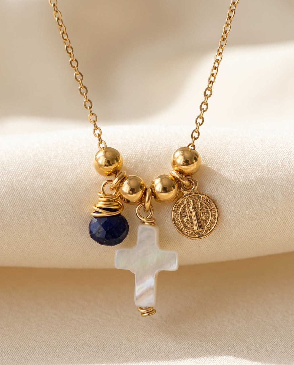 Detalle de la cruz de concha nácar, la medalla de San Benito chapada en oro y la piedra azul del collar Perla Santa