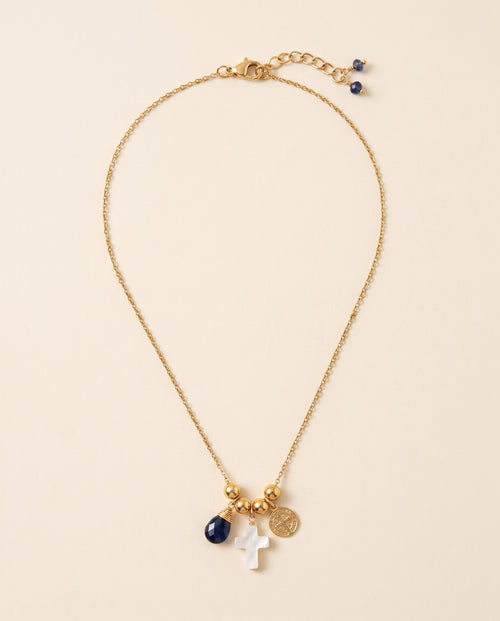 Collar Perla Santa de cadena dorada con cruz de concha nácar, medalla de San Benito y piedra azul facetada, sobre fondo crema