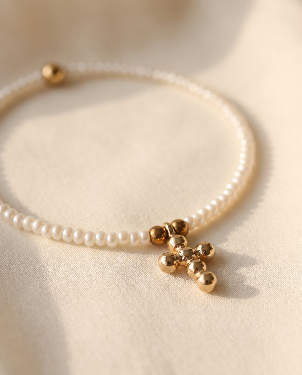 Detalle de la cruz de chapa de oro y las perlas naturales de la pulsera Perla Santa