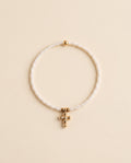 Pulsera de perla natural blanca con cruz de chapa de oro sobre fondo crema, Perla Santa