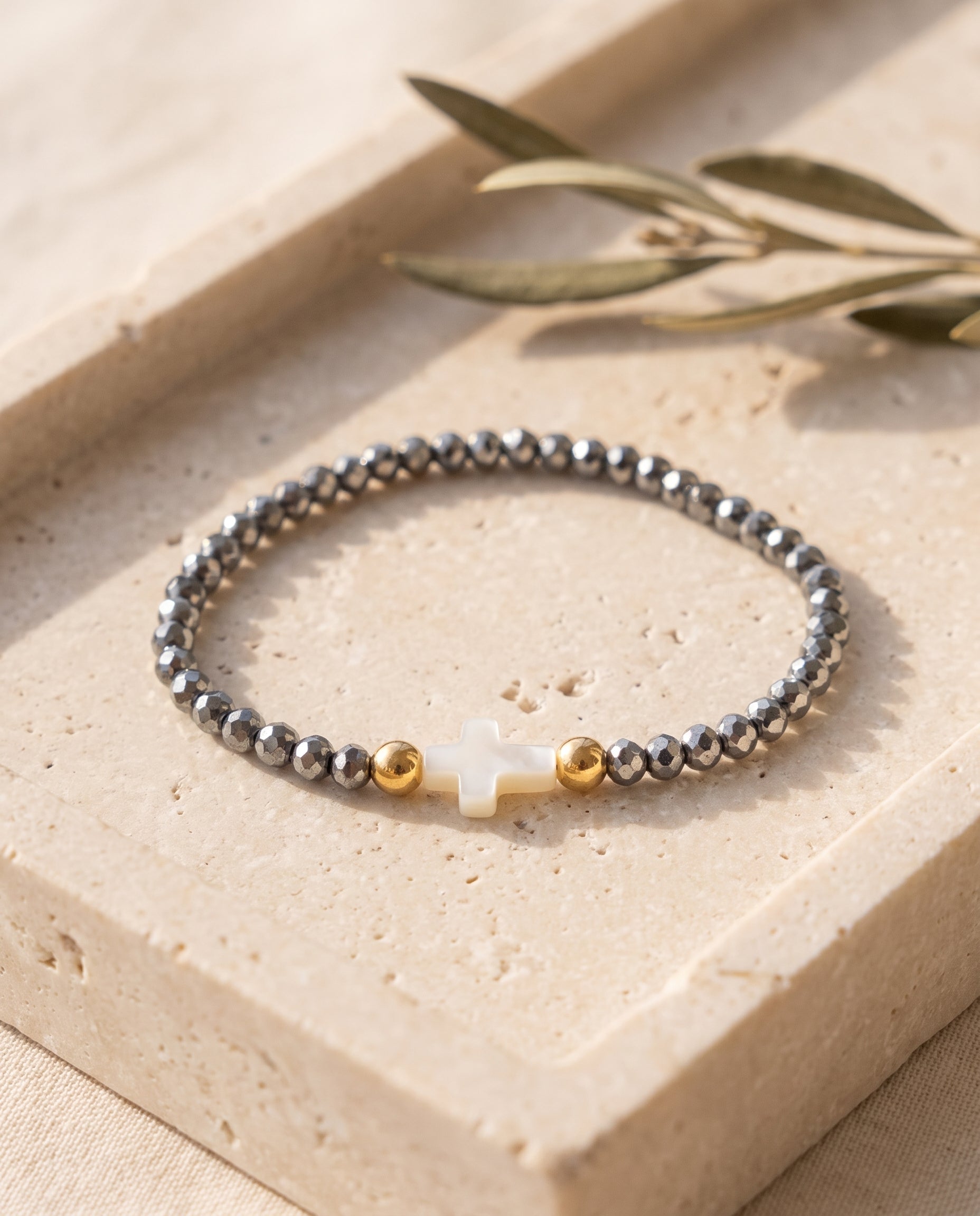 Pulsera con cruz de concha nacar sobre bandeja de piedra beige con rama de olivo, Perla Santa