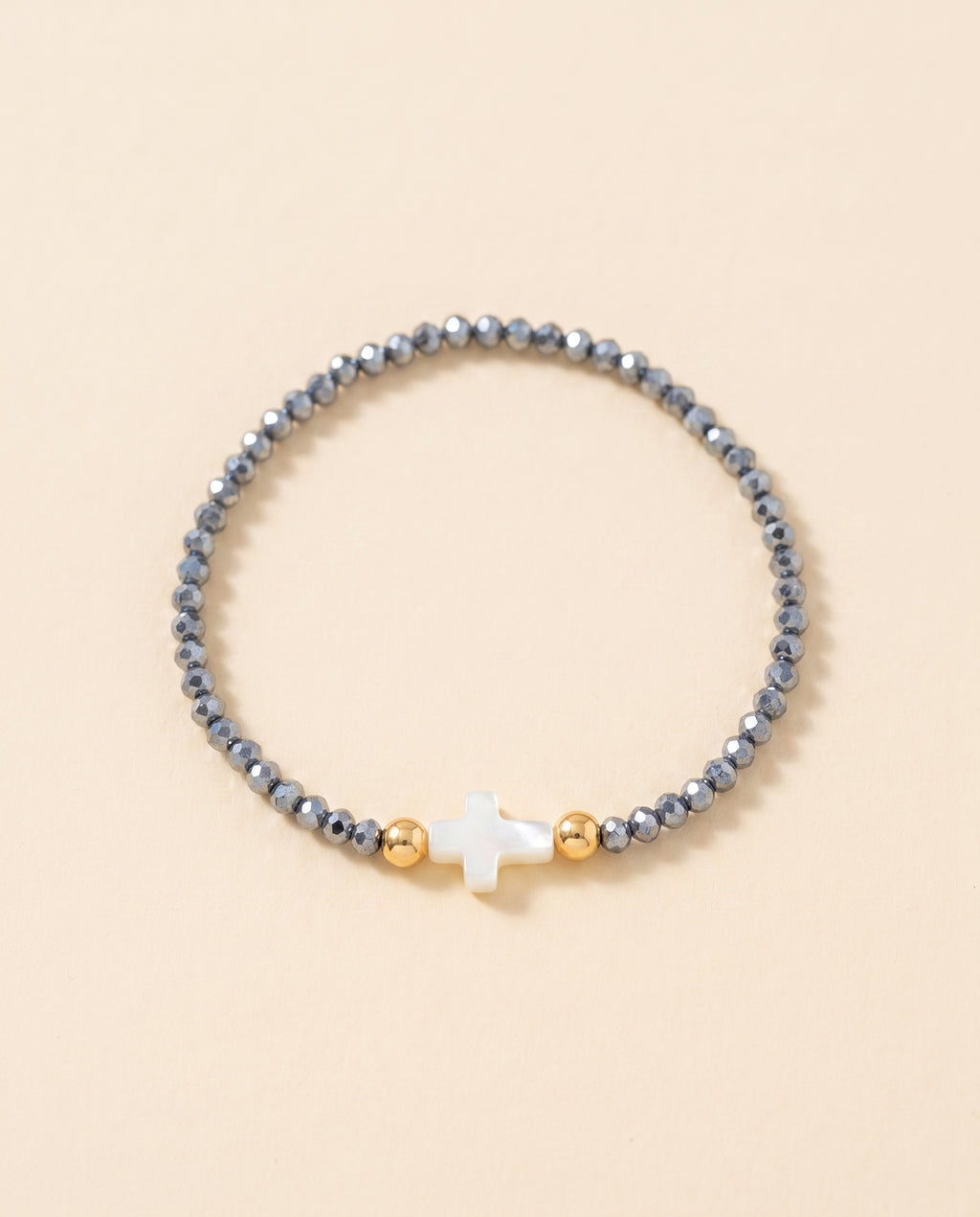 Pulsera de cristal facetado azul acero con cruz de concha nacar sobre fondo crema, Perla Santa