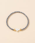 Pulsera de cristal facetado azul acero con cruz de concha nacar sobre fondo crema, Perla Santa
