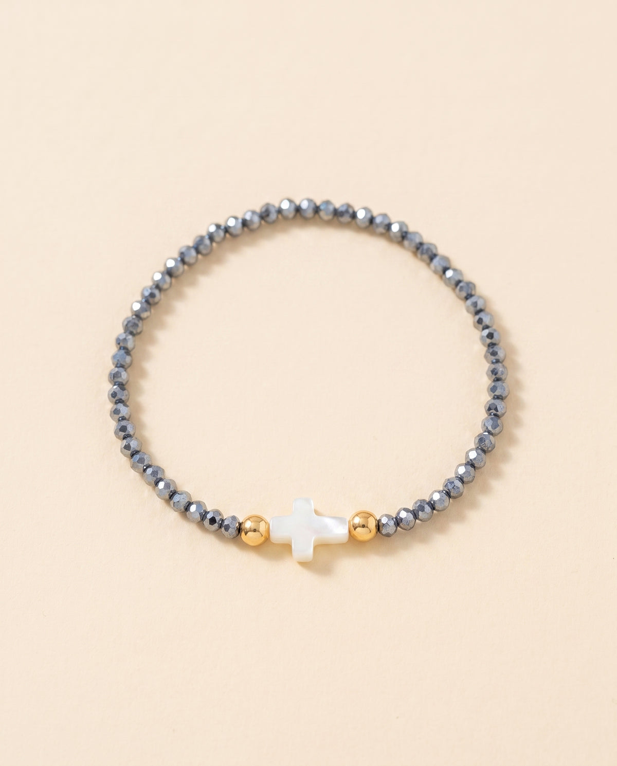 Pulsera de cristal facetado azul acero con cruz de concha nacar sobre fondo crema, Perla Santa