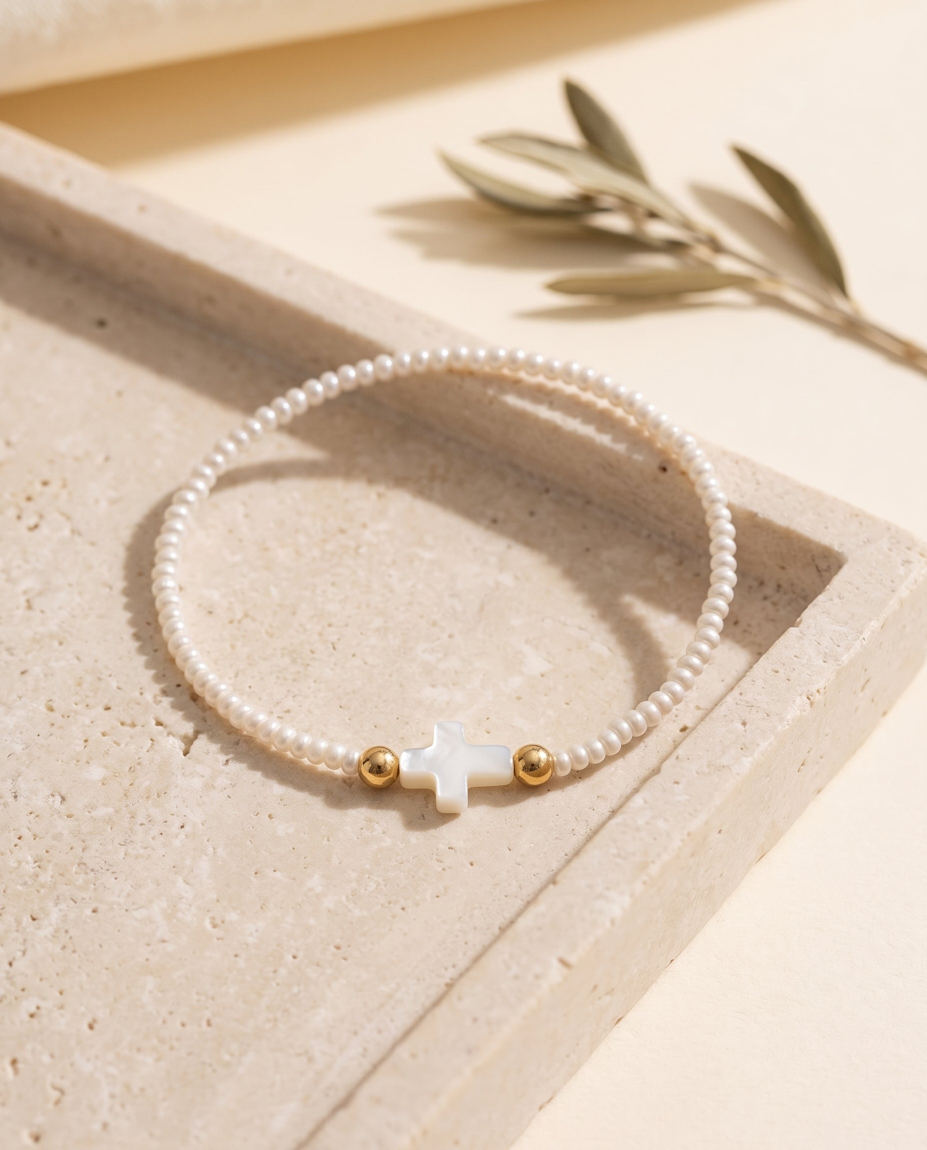 Pulsera de perla con cruz de concha nacar sobre bandeja de piedra beige con rama de olivo, Perla Santa