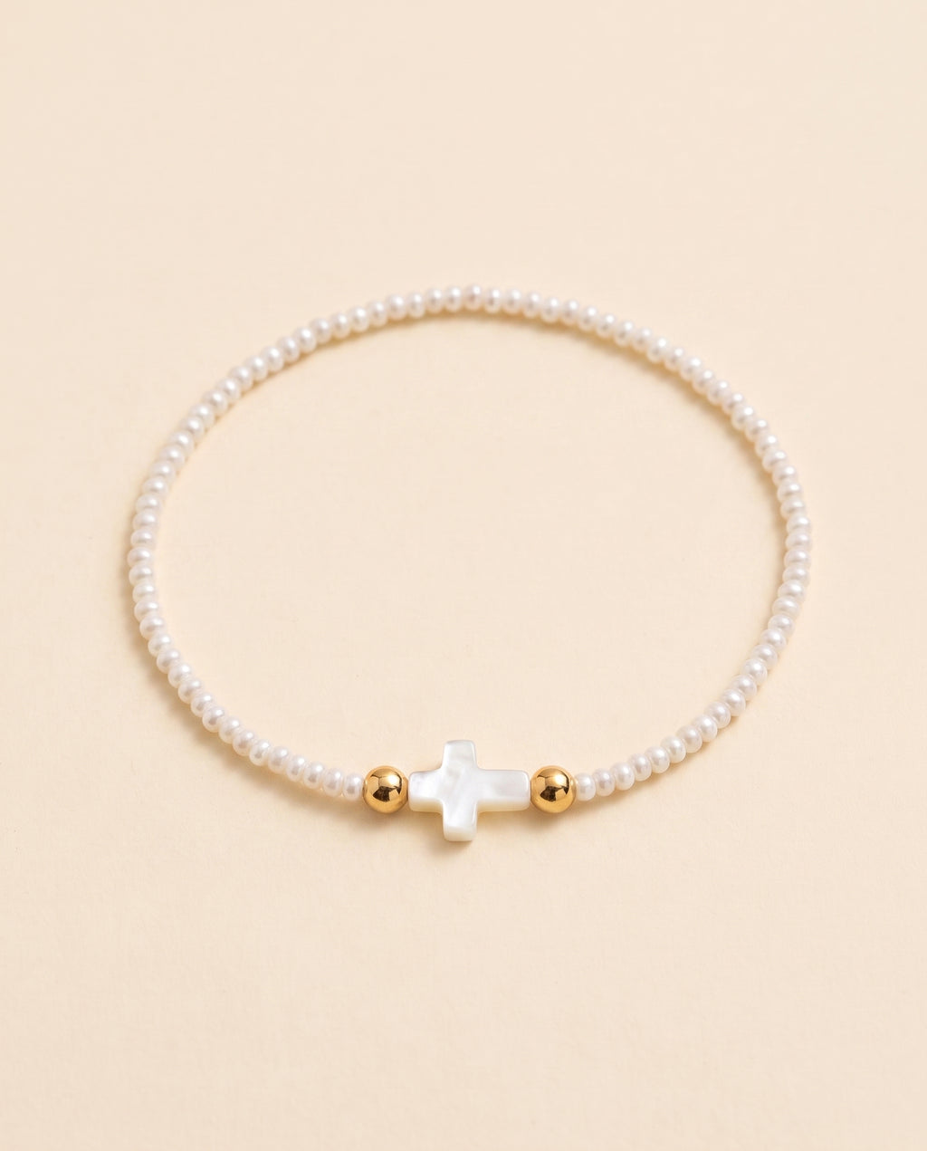 Pulsera de perla natural blanca con cruz de concha nacar sobre fondo crema, Perla Santa