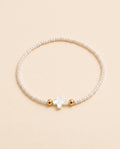 Pulsera de perla natural blanca con cruz de concha nacar sobre fondo crema, Perla Santa
